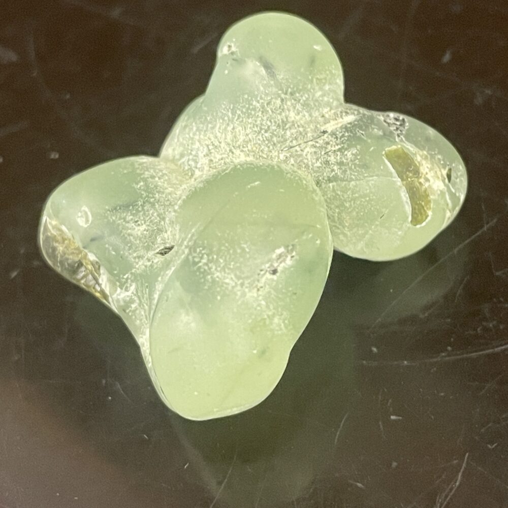 A translucent, pale green tumbled Prehnite stone (21.18g / 0.747oz) with bubble-like formations on a dark surface.