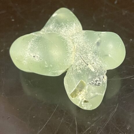 A Prehinite natural-shaped, tumble-polished 21.18g (.747 oz) stone on a dark background, highlighting its pale green color.