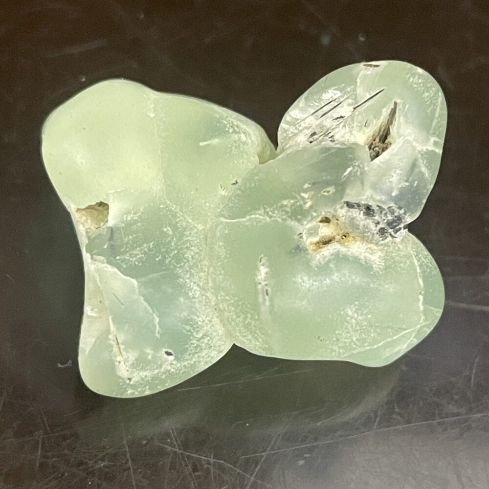 The Prehinite Natural Shaped Tumble Polished specimen (21.18 grams/.747 oz) features pale green, translucent, fractured surfaces on a dark background.
