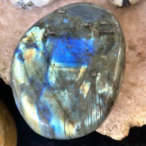 Labradorite display specimen with outstanding gold, bronze, and blue iridescence on a smooth surface, set on beige background.